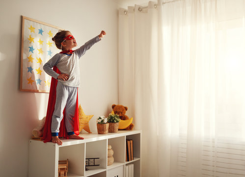 Child Girl In A Super Hero Costume With Mask And Red Cloak .