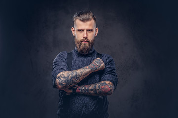 Portrait of a handsome old-fashioned hipster in a blue shirt and suspenders, standing with crossed...