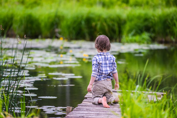 Fototapeta na wymiar the boy kneels on a wooden bridge on the river and looks into the water