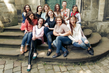 Obraz na płótnie Canvas young happy women sitting on stairs posing on background of old european city street, stylish hipster girls, moments of happiness, friendship concept
