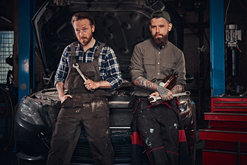 Fototapeta na wymiar Two mechanic sit on a broken car, rest after a hard day's work in a garage.