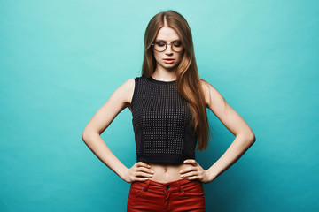 Fototapeta na wymiar Sexy and fashionable model girl with slim sporty figure in black t-shirt, red pants and in stylish round glasses, isolated at green background