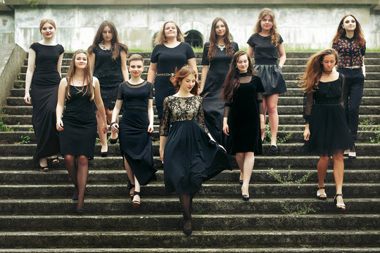 gorgeous women group in black dresses posing walking down the stairs in the city. stylish lady party with gothic theme. elegant girls