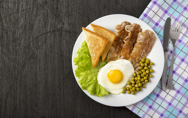 Egg and bacon on lettuce leaves with green peas in a white plate and on a black wooden background with a cloth napkin. With space for writing.