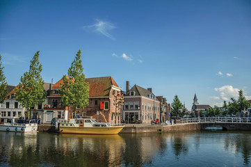Wide canal with brick houses, boats moored on its bank reflected in water and blue sky of sunset in Weesp. Quiet and pleasant village full of canals and green near Amsterdam. Northern Netherlands.
