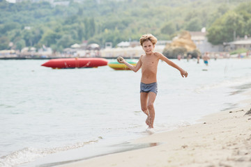 Naklejka na ściany i meble Smiling boy enjoying summer vacation and playing on the beach