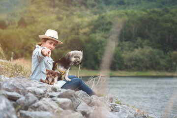 Young woman sitting with her dogs beside the river pointing at camera in evening.