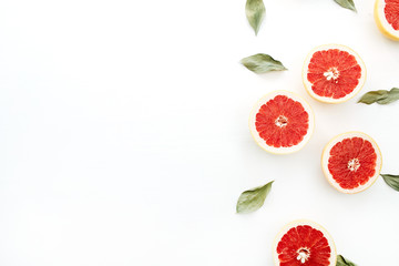 Red sliced grapefruits and green leaves on white background. Flat lay, top view food concept.