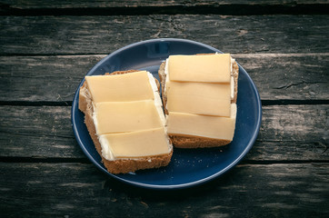 Sandwich with cheese and butter on the blue plate. Rustic kitchen. Simple breakfast. Fast food.