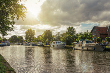 Fototapeta premium Wide tree-lined canal with houses and boat moored on its bank on sunset at Weesp. Quiet and pleasant village full of canals and green near Amsterdam. Northern Netherlands. Retouched photo.