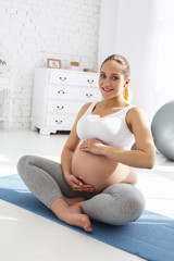 Meditation for mom. Merry pregnant woman meditating while grinning to camera