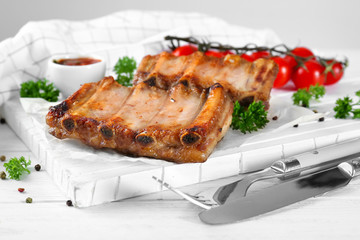 Wooden board with delicious grilled ribs on table