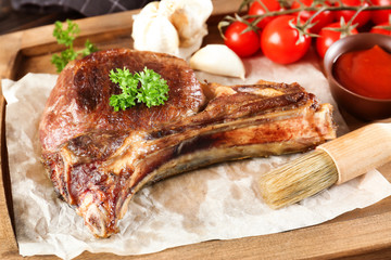 Wooden plate with delicious ribs, tomatoes and sauce on table