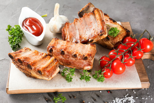 Wooden board with delicious grilled ribs, tomatoes and sauce on table