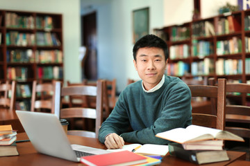 Asian student with laptop studying in library