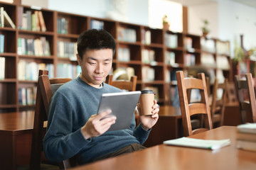Asian student with tablet studying in library