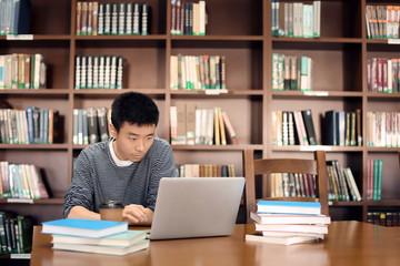 Asian student with laptop studying in library