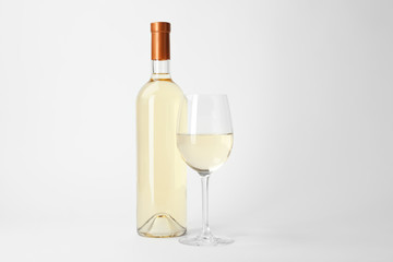 Bottle and glass of expensive white wine on light background