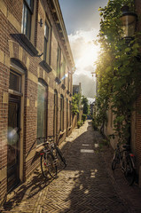 Alleyway with brick houses, bikes and bright sunset light in Weesp. Quiet and pleasant village full of canals and green near Amsterdam. Northern Netherlands. Retouched photo.