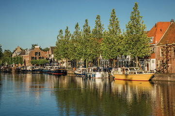 Wide canal with brick houses, boats moored on its bank reflected in water and blue sky of sunset in Weesp. Quiet and pleasant village full of canals and green near Amsterdam. Northern Netherlands.