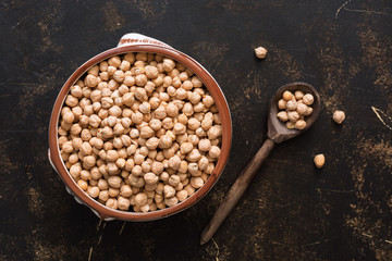 Raw chickpeas in a ceramic bowl and a wooden spoon on a dark background. View from above.