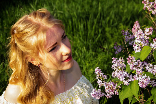 Beautiful blonde girl about something thinking looking at the flowers of lilac.