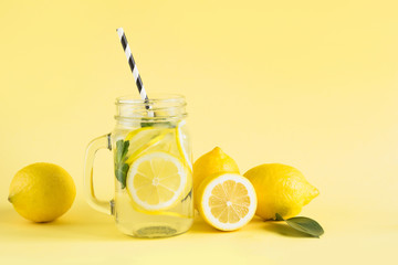 Fresh summer fruits water or lemonade with lemon and mint on yellow background. Close up.