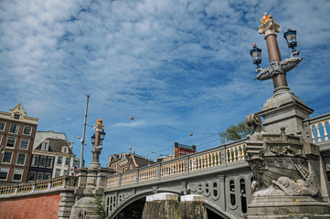 Fototapeta na wymiar Stone bridge over canal decorated by sculpture of ship's bow and elegant light post in Amsterdam. The city is famous for its huge cultural activity, graceful canals and bridges. Northern Netherlands.