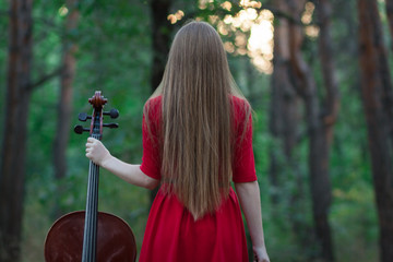 Woman in red dress with cello in the forest
