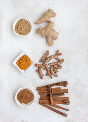 Three healthy spices (turmeric, ginger and cinnamon) in white bowls on white concrete background
