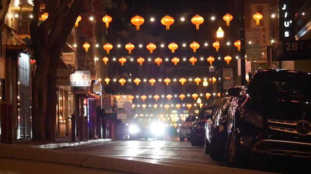 Chinese lanterns strung across a street as a car drives towards the camera in slow motion.