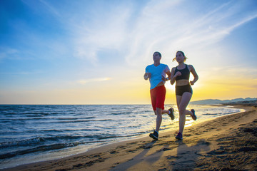 Man and women running on tropical beach at sunset