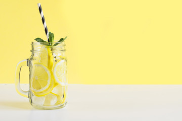 Fresh summer fruits water or lemonade with lemon and mint on yellow background. Close up.