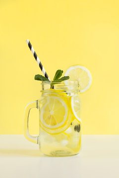 Fresh summer fruits water or lemonade with lemon and mint on yellow background. Close up.