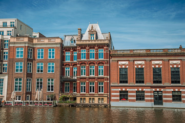 Fototapeta na wymiar Old brick buildings facade and restaurant along the canal and sunny blue sky in Amsterdam. The city is famous for its huge cultural activity, graceful canals and bridges. Northern Netherlands. 