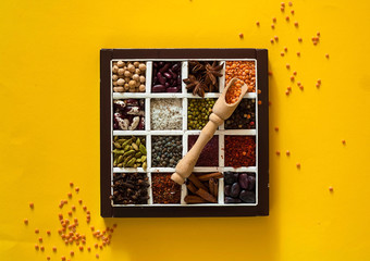 The concept of cereals organic products and spices on yellow background. Seasonings for eating,beans for cooking,healthy diet, choice of clean food, copy space, closeup,top view.