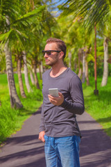 Fototapeta na wymiar Man using cellphone / smartphone in tropical environment.