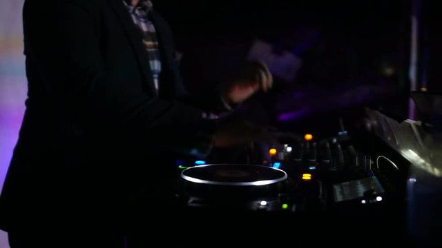 Professional deejay mixing tracks on turntable at nightclub, switching controls