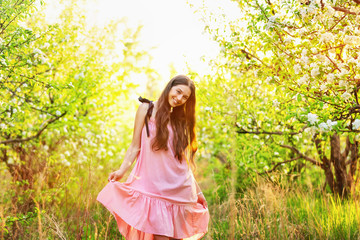 Fototapeta na wymiar Beatiful smiling girl in pink dress is walking along blooming apple spring garden.