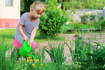 A small pretty girl in the garden watered plant from a green watering can. Spring and summer. Nature blossomed. Gardening. STEM. Growing plants. Biology lesson.