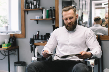 Portrait of handsome bearded man with fashionable hairstyle and beard at barber shop. He chooses a haircut in the journal.