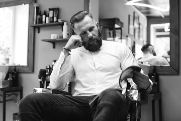 Portrait of handsome bearded man with fashionable hairstyle and beard at barber shop. He chooses a haircut in the journal.