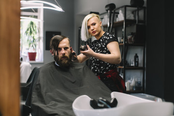 Stylish hairdresser cutting hair of client at barber shop. Beard man getting haircut at salon.