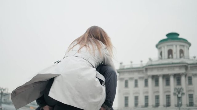 Man with stubble and headphones on neck carrying his beautiful woman in cap on back having journey trip, trendy stylish joyful couple hugging having meeting outdoors foggy day
