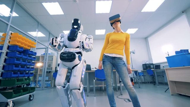 Human-like robot and a young woman in virtual glasses are dancing.