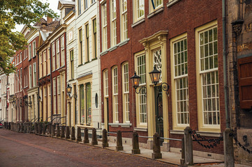 Fototapeta na wymiar Quiet street with elegant semi-detached brick buildings and lamps at the end of the day in Delft. Calm and graceful village full of canals and Gothic architecture. Western Netherlands.