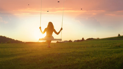 SILHOUETTE: Unrecognizable young woman swaying on swing at golden summer sunset - obrazy, fototapety, plakaty