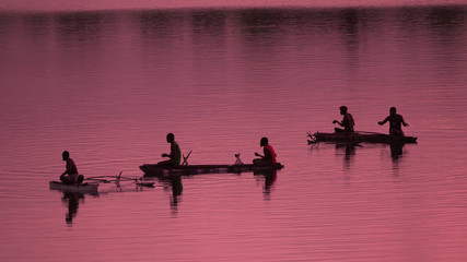 Naklejka premium SILHOUETTE Unrecognizable local fishermen fishing in small boats at pink sunrise