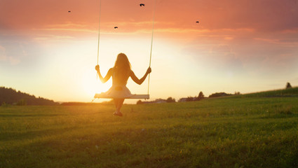 SILHOUETTE: Unknown girl swaying on wooden swing at golden sunset in spring - obrazy, fototapety, plakaty