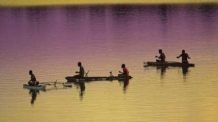 Unrecognizable local fishermen fishing in small wooden boats at colorful sunrise